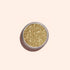 A round container of Manucurist Golden Chrome Powder, filled with shiny gold glitter and viewed from above on a light beige background, highlights its shimmering allure.