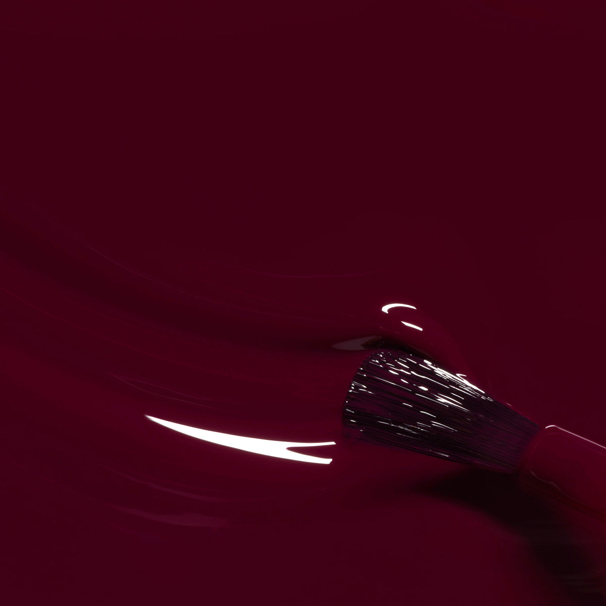 A close-up of a Manucurist brush applying Prune nail polish, a glossy red wine shade, with velvet reflections shimmering on the wet surface.
