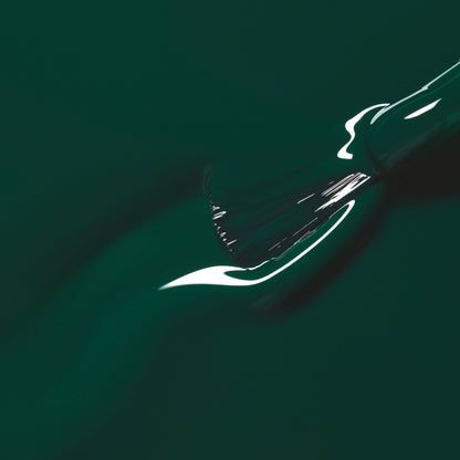 A close-up of a paintbrush applying Manucurist’s Emerald, a rich gemstone-inspired green shade, creating a smooth, glossy streak on the surface.