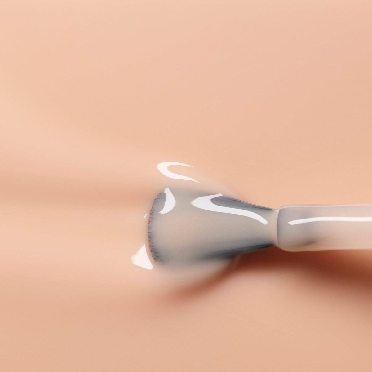 A makeup brush glides Manucurist Beige foundation onto light skin, creating a glossy, even finish—just like the flawless effect of nude polish.