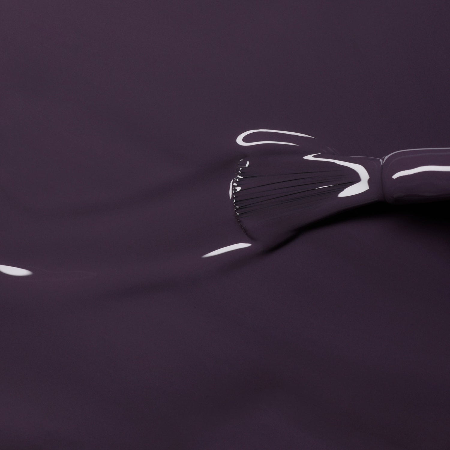 A close-up of a Manucurist brush spreading Queen of Night, a smooth, glossy dark violet Green Flash gel nail polish, across a surface with visible bristle marks and highlights.