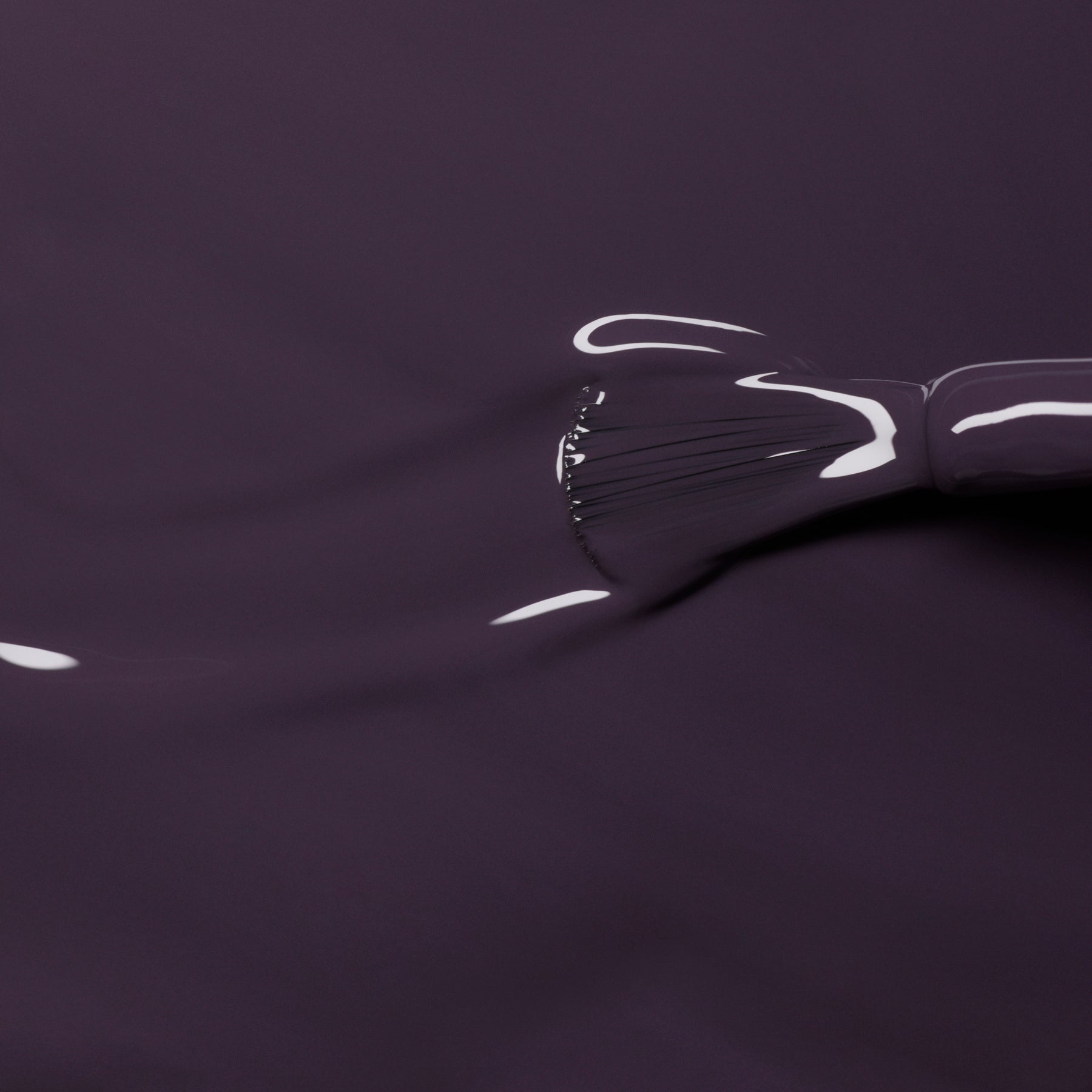 A close-up of a Manucurist brush spreading Queen of Night, a smooth, glossy dark violet Green Flash gel nail polish, across a surface with visible bristle marks and highlights.
