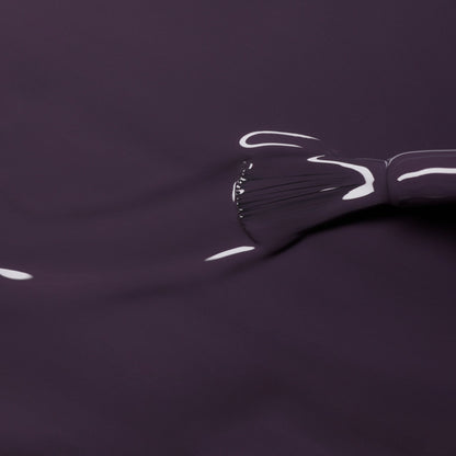 A close-up of a Manucurist brush spreading Queen of Night, a smooth, glossy dark violet Green Flash gel nail polish, across a surface with visible bristle marks and highlights.