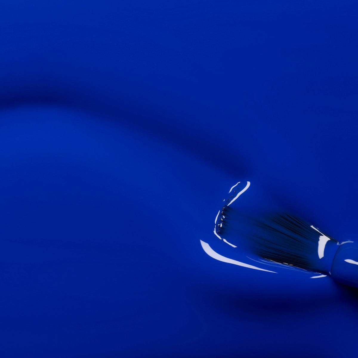 A close-up of a paintbrush applying Manucurist’s Ultramarine nail polish, showcasing its smooth, glossy electric blue finish as light reflects off the wet surface.