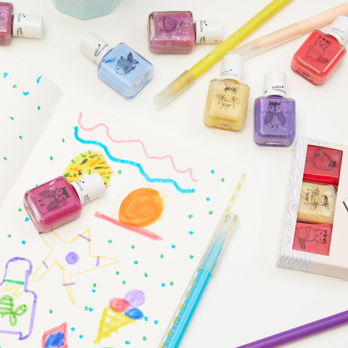 An open sketchbook with colorful doodles is surrounded by bright pens and Manucurist kids&