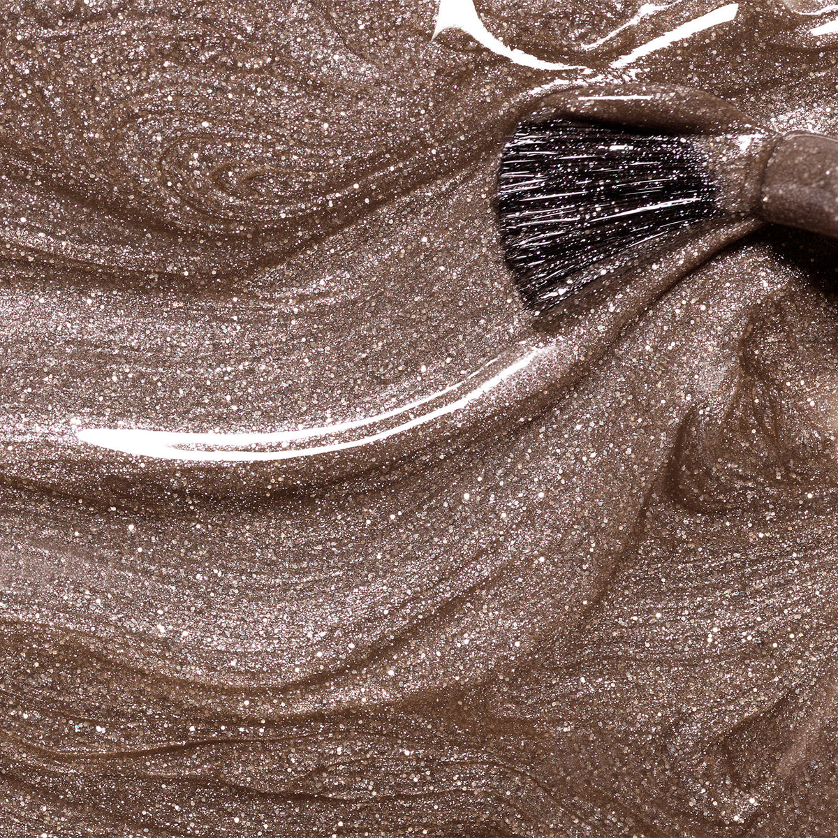 A close-up of a brush swirling through Manucurist’s Quartz nail polish, revealing fluid, metallic bronze patterns and glossy, shimmery highlights.
