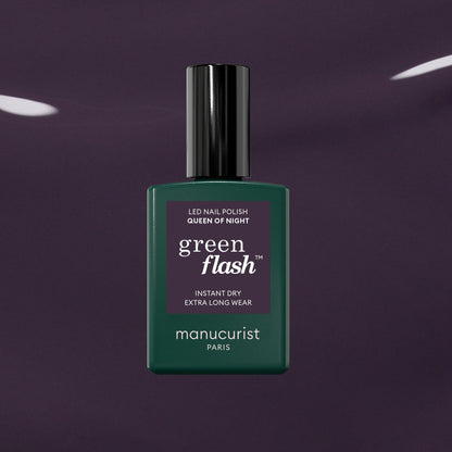 A bottle of Manucurist Queen of Night gel nail polish stands against a dark, glossy backdrop. The bottle features a deep green shade, black cap, and crisp white text on the label.