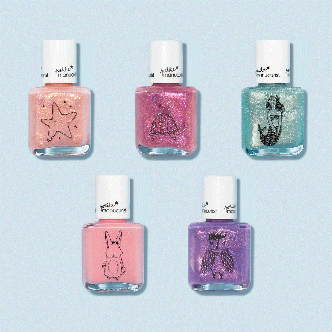 Five bottles of Customisable Rainbow Petite Manucurist kids nail polish by Manucurist, each with a white cap and cute black outline (starfish, turtle, mermaid, bunny, and owl), are arranged on a light blue background.