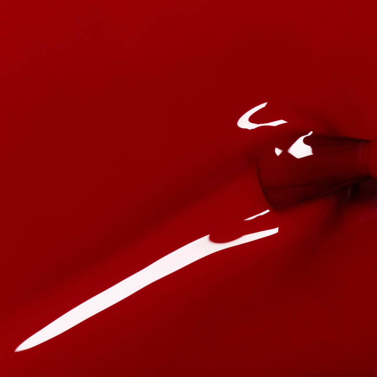 A close-up of Manucurist’s Red Velvet nail polish being poured, creating smooth, glossy waves and reflections. The abstract image showcases a vibrant, fluid look with an intense velvet red color.