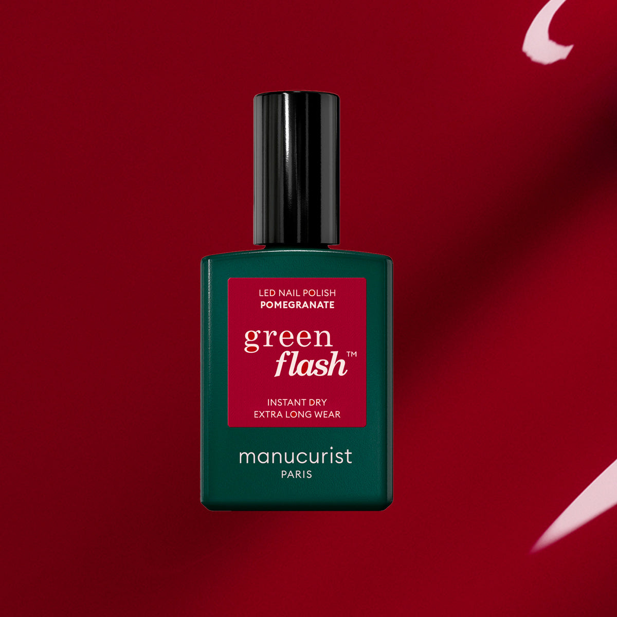 A green Manucurist bottle of Pomegranate gel polish sits on a deep red background with a white brushstroke. The label showcases its instant dry and extra long wear features.