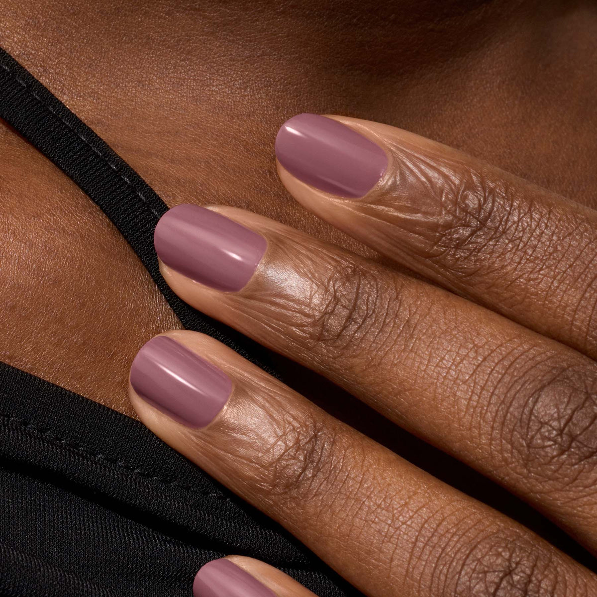 A close-up of a hand with medium-dark skin tone resting on a shoulder, nails manicured and painted with Manucurist&