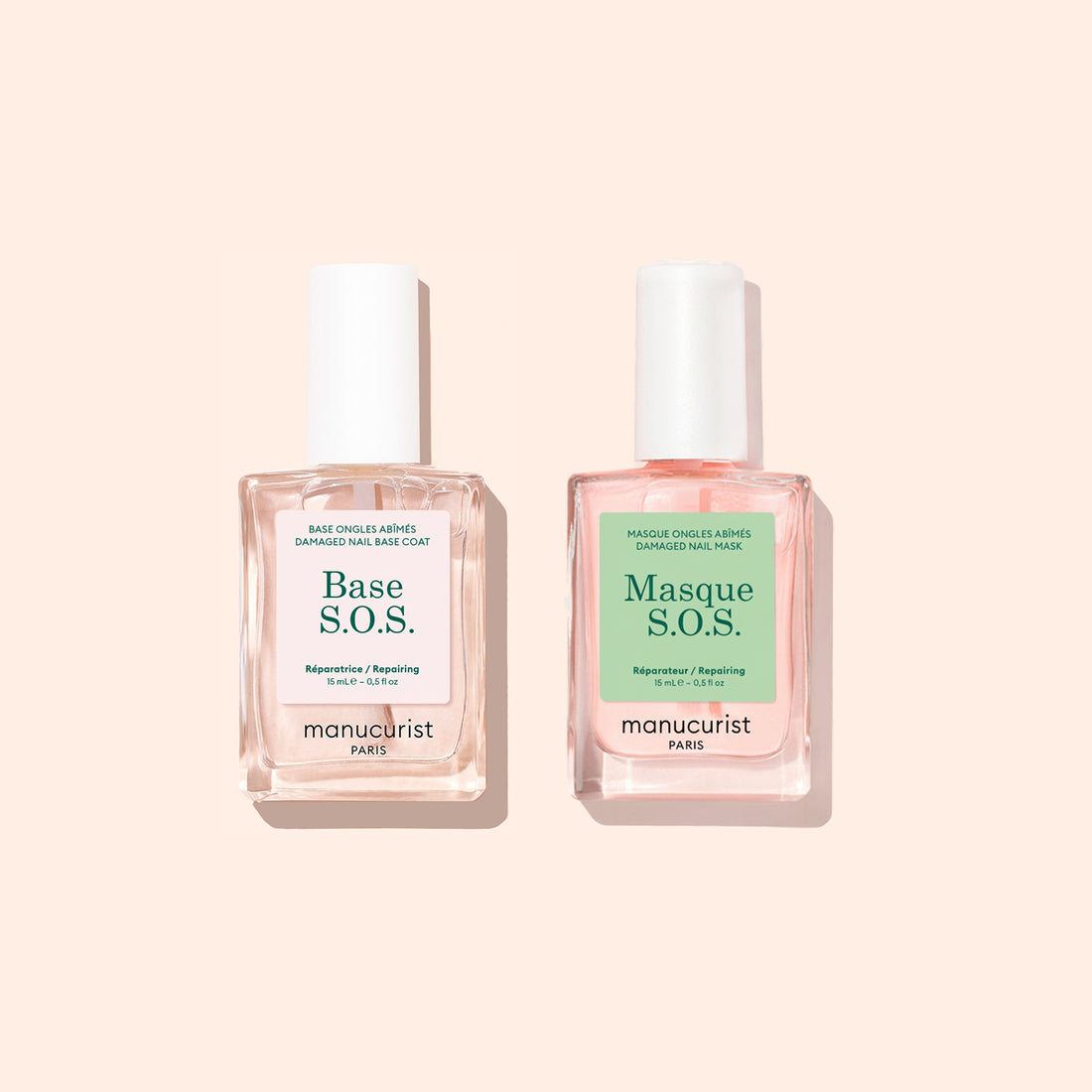 Two square glass bottles with white caps contain pink nail care liquids from Manucurist’s Basic Routine - Damaged Nails set, designed to repair and strengthen brittle nails. The left bottle is labeled Base S.O.S., and the right is labeled Masque S.O.S. Both products are by Manucurist, shown on a light beige background.
