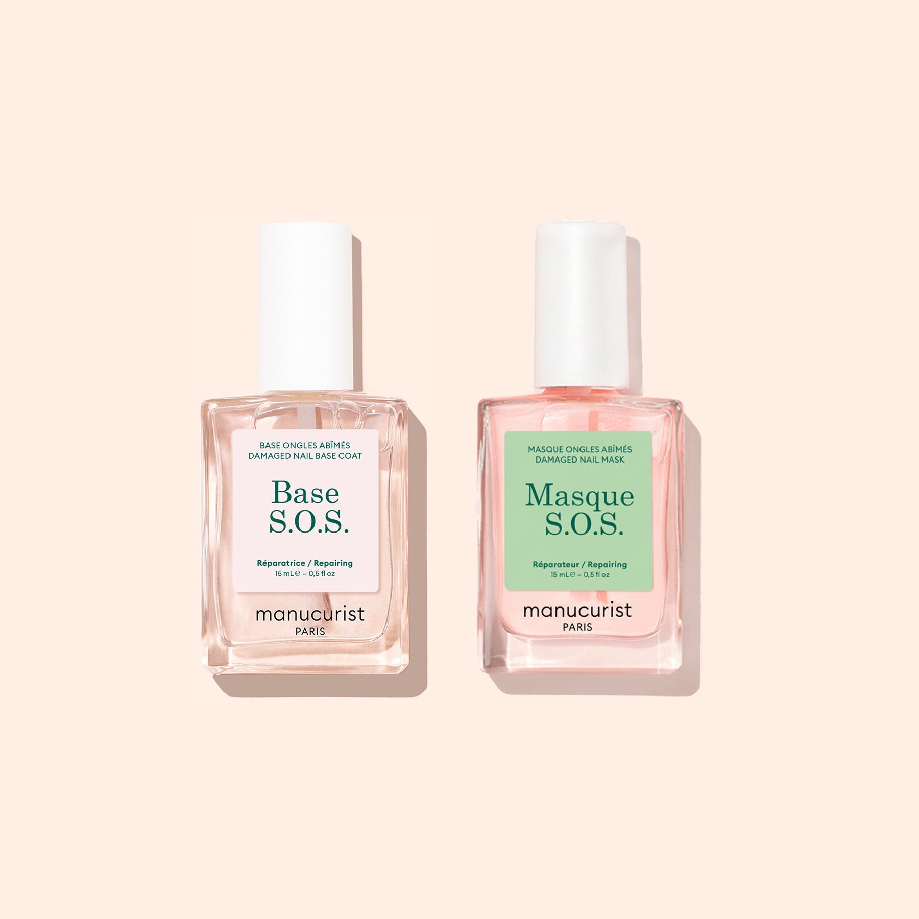 Two square glass bottles with white caps contain pink nail care liquids from Manucurist’s Basic Routine - Damaged Nails set, designed to repair and strengthen brittle nails. The left bottle is labeled Base S.O.S., and the right is labeled Masque S.O.S. Both products are by Manucurist, shown on a light beige background.