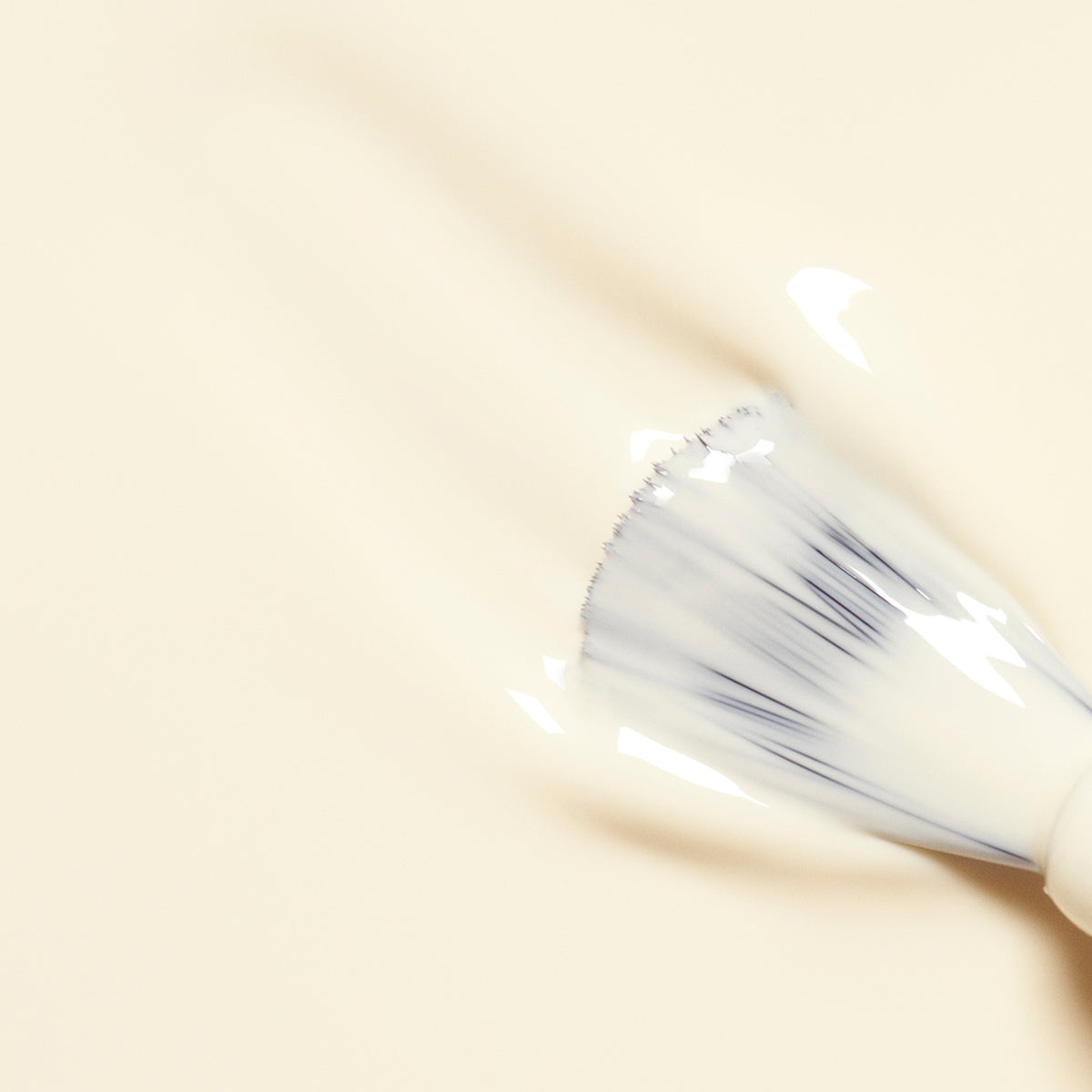 A close-up of the Manucurist Shell brush gliding creamy, light beige polish across a surface, creating soft, textured strokes.
