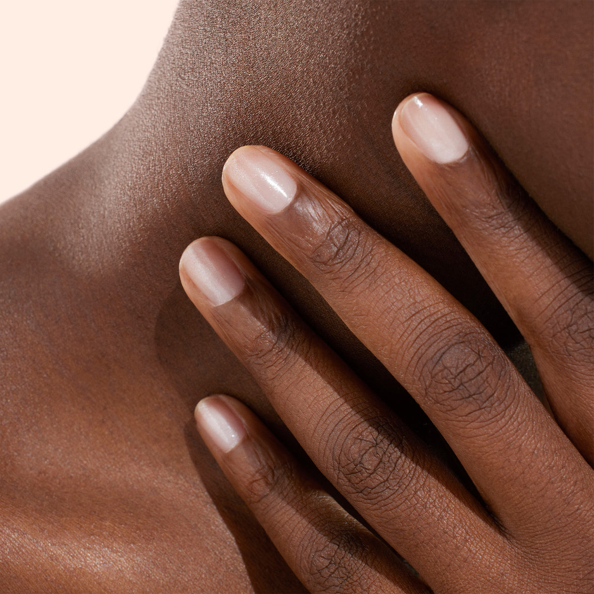 A close-up of a hand with neatly manicured nails, painted in Manucurist’s Active™ Shine Opal plant-based nail polish, resting gently on the neck and collarbone of a person with smooth, dark skin.
