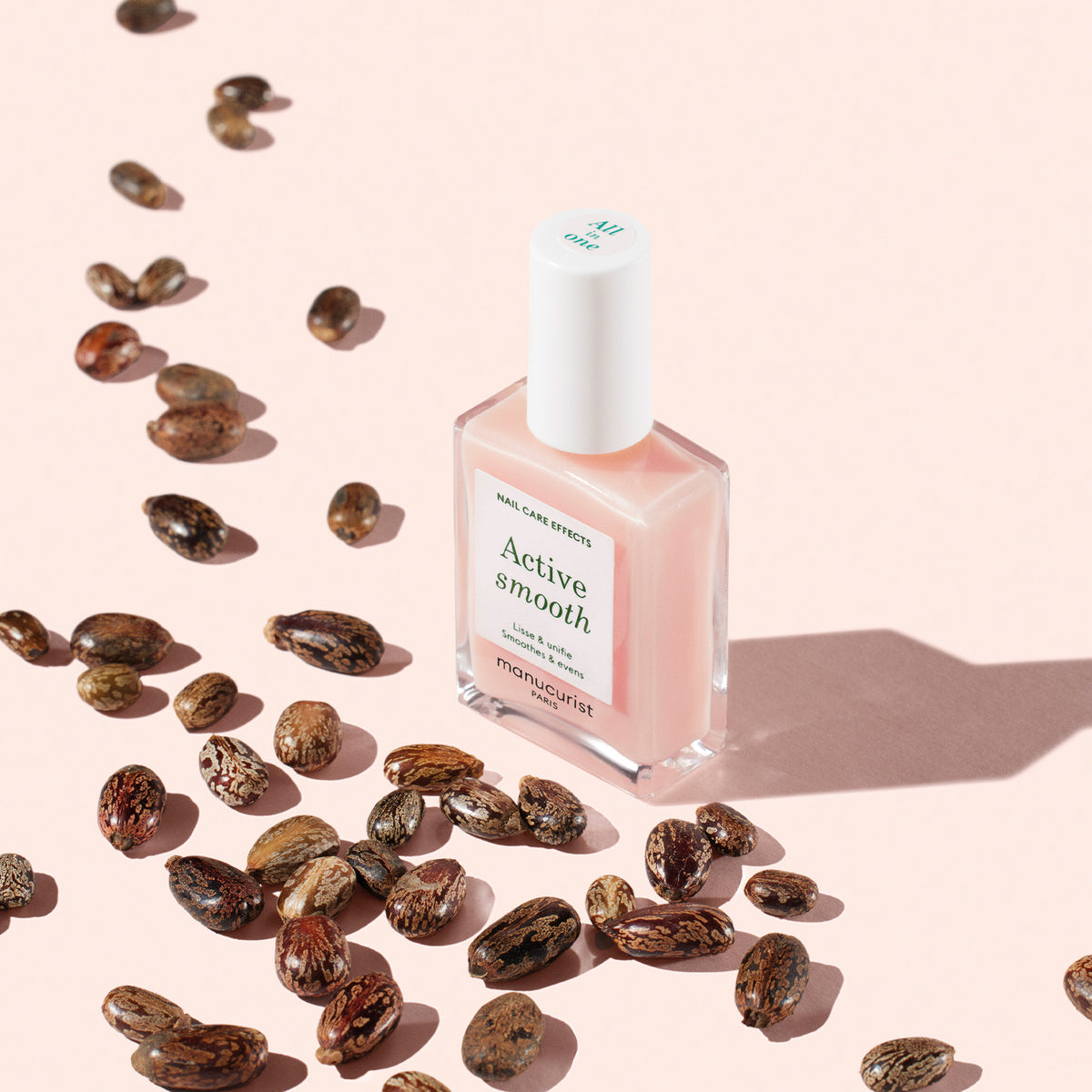 A bottle of Manucurist Active™ Smooth 00 pink nail polish rests on a light pink surface, surrounded by scattered brown seeds casting delicate shadows—making it an ideal choice for anyone looking for a nail care essential or a CC Polish Treatment to perfect their look.