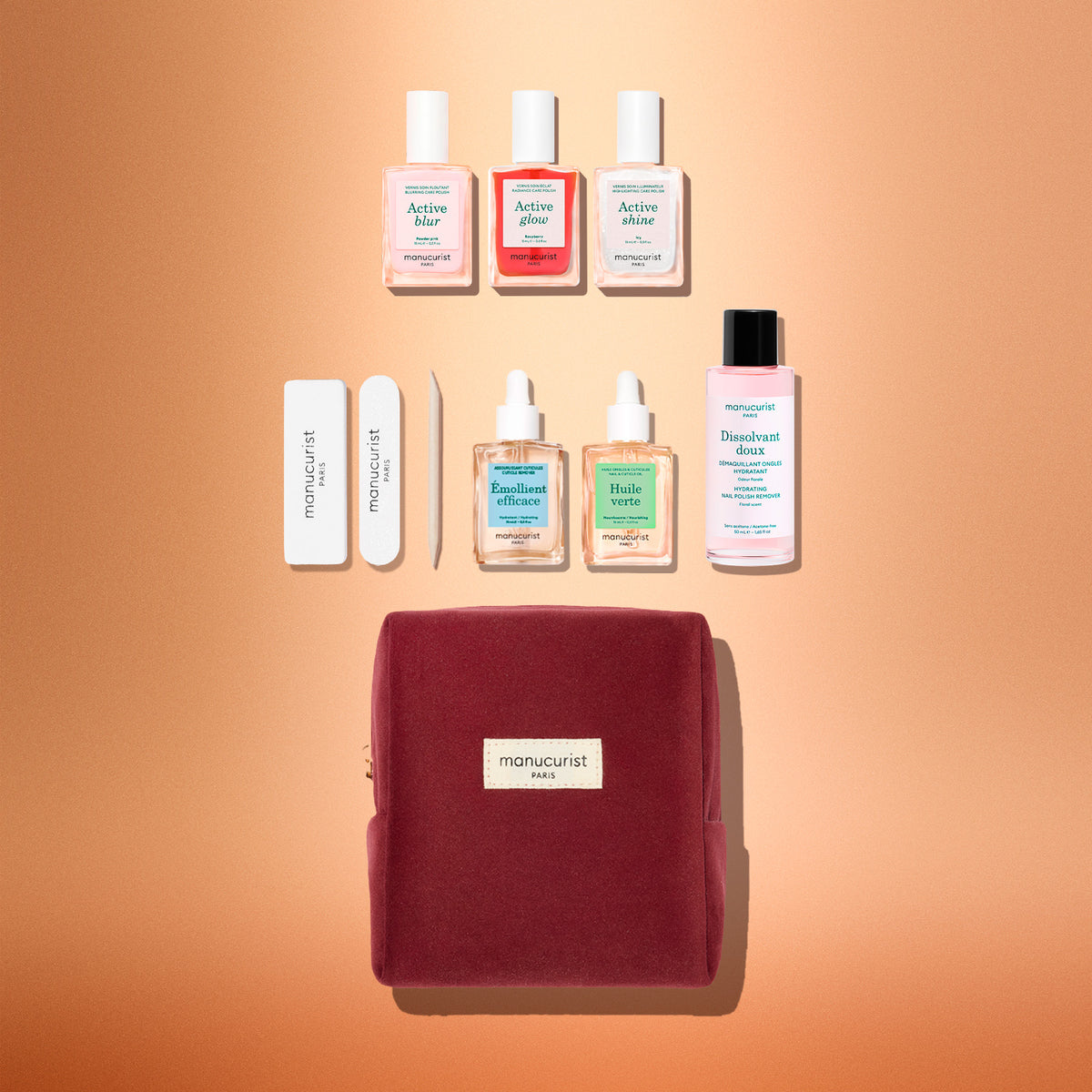The Manucurist Active™ Starter Kit Gift Set includes three nail polishes, two glass droppers, two nail files, a cuticle pusher, and polish remover arranged above a zippered burgundy pouch.