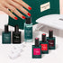 A manicured hand with red nails appears beside the Manucurist Starter Kit, featuring nail polish bottles, remover, nail clips, a UV lamp, and a green pouch—neatly arranged on a light surface for an ultra-glossy manicure.