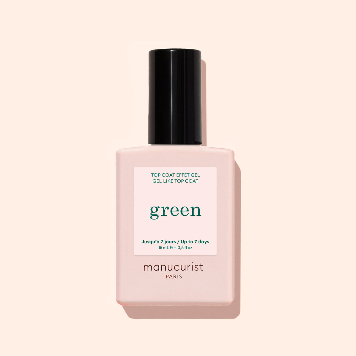 A bottle of Manucurist Sunshine Top Coat, a plant-based, high-shine, long-wear gel-effect nail polish, features a pale pink base and black cap against a beige background.