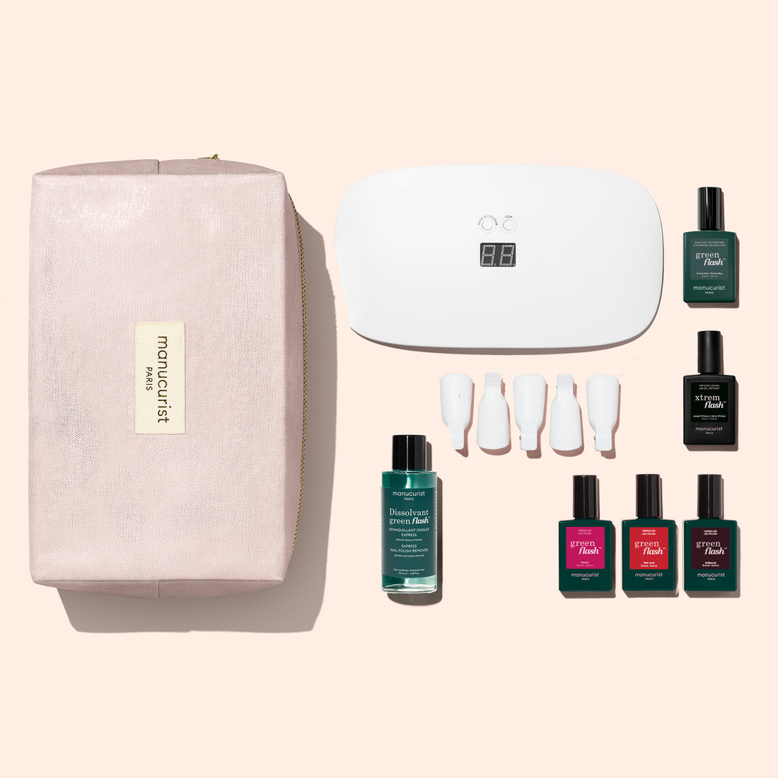 Introducing the Manucurist Starter Kit: a complete gel polish set with everything you need for an ultra-glossy, salon-quality manicure at home. The kit includes a chic pink pouch, an LED nail lamp, four white nail tips, nail polish remover, and five bottles of vibrant gel polish in assorted colors—all arranged neatly on a beige background. Plus, it features a nourishing vitaminized base coat to care for your nails while you create stunning looks.