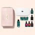 The Manucurist Starter Kit includes a pink pouch, four bottles of nail polish (with one vitamin-infused base coat), a remover bottle, green nail clips, a white LED nail lamp, and a remover solution—all elegantly displayed on a pale pink background for the perfect gel manicure set.