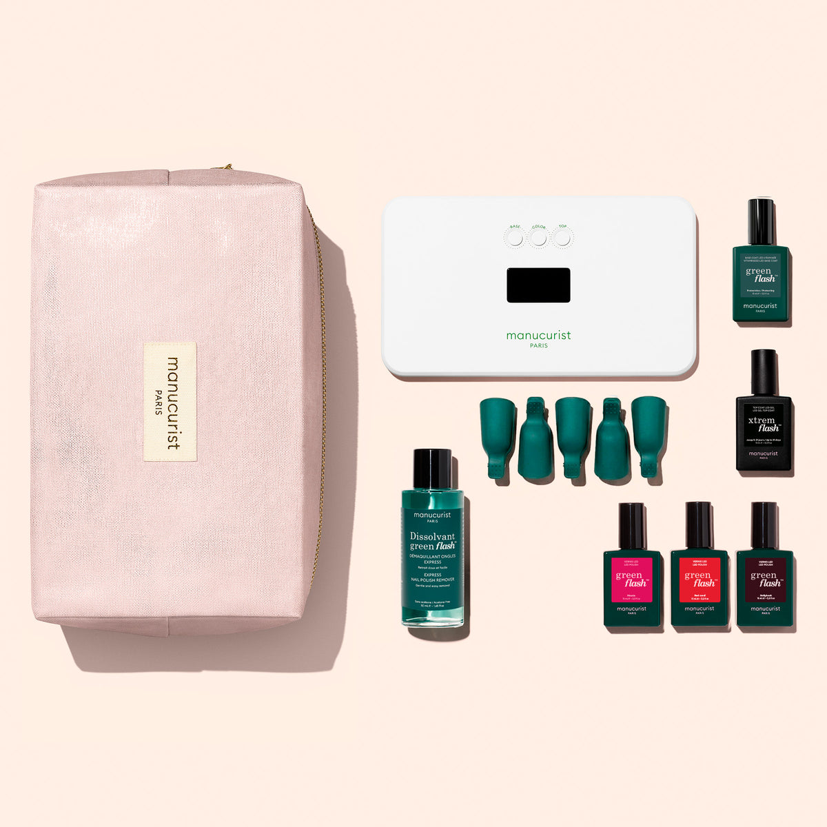 The Manucurist Starter Kit features a pink pouch with a gold label, a white LED nail lamp, a green nail polish remover bottle, four green nail clips, and six green and red nail polish bottles—including the Green Flash gel polish—all neatly arranged on a light background to form a complete gel polish kit.