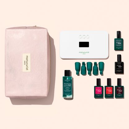 The Manucurist Starter Kit features a pink pouch with a gold label, a white LED nail lamp, a green nail polish remover bottle, four green nail clips, and six green and red nail polish bottles—including the Green Flash gel polish—all neatly arranged on a light background to form a complete gel polish kit.
