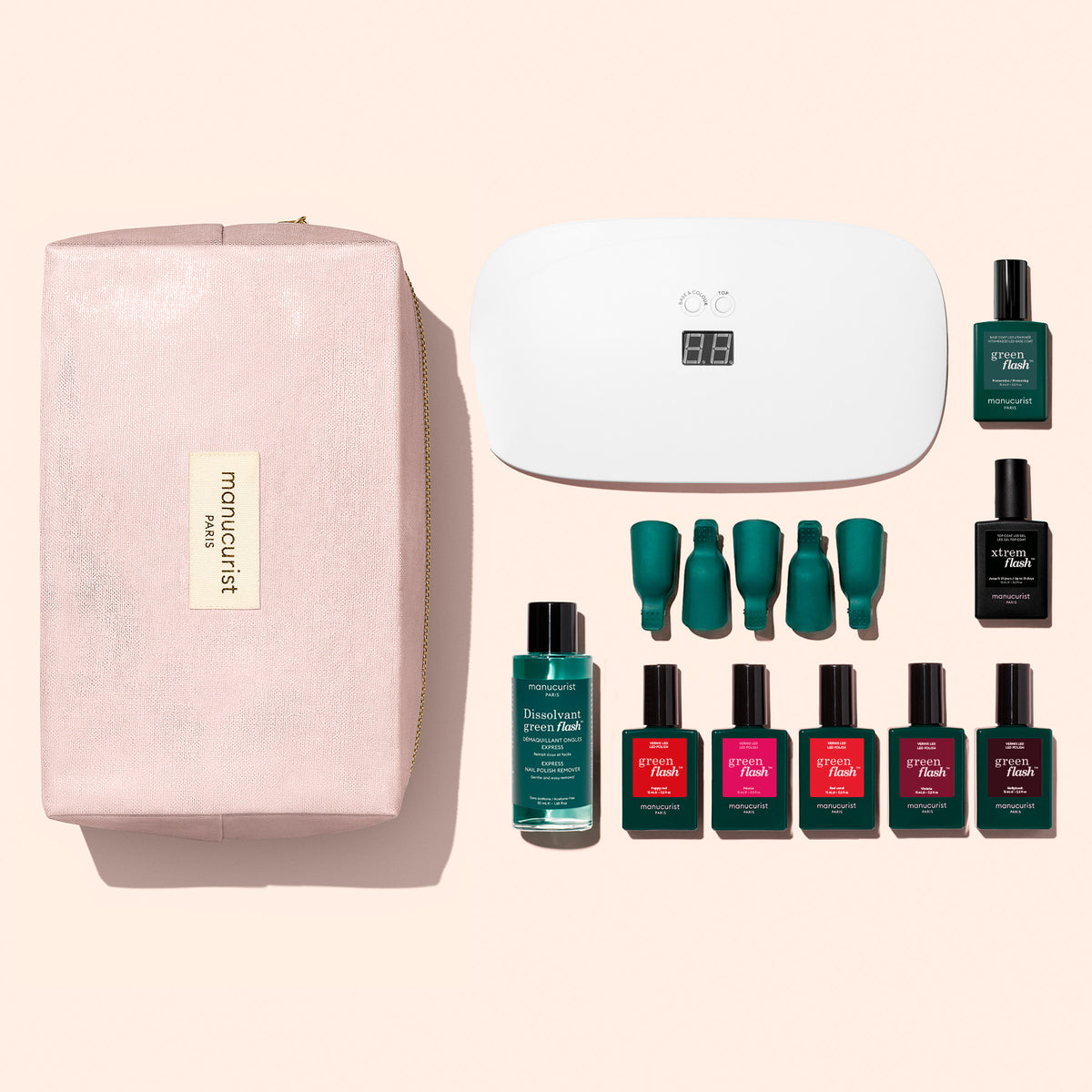 The Manucurist Super Starter Kit features a pink cosmetic bag, a white LED nail lamp, six bottles of Green Flash gel polish in green and red shades offering up to 21 days’ wear, a remover bottle, a vitaminized base coat, and four nail polish caps—all displayed on a light background.
