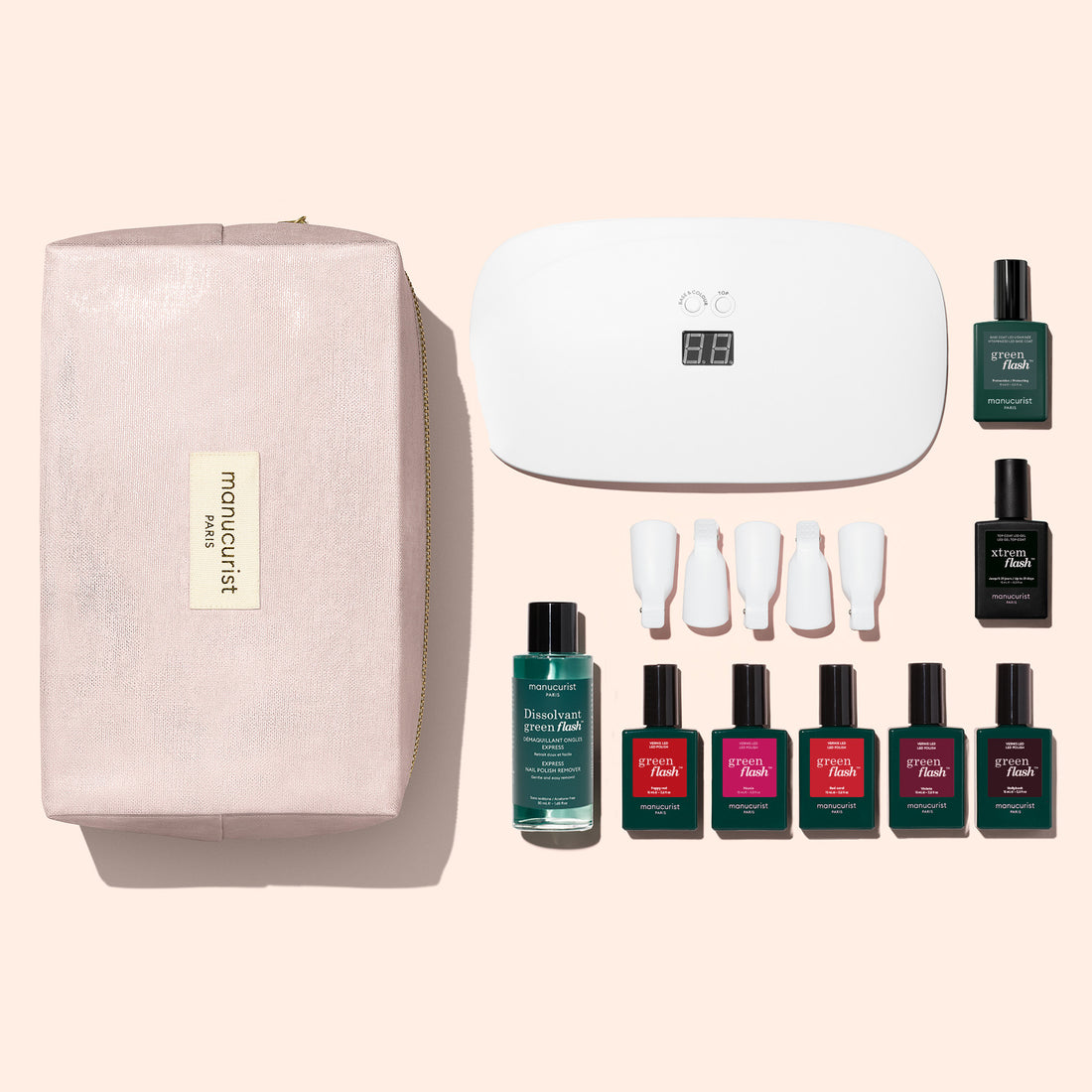 The Manucurist Super Starter Kit features a pink makeup bag, a white LED nail lamp, four nail polish bottles—including a vitamin-enriched base coat—four nail tips, and a bottle of polish remover, all neatly arranged on a soft pink background for the perfect ultra-glossy manicure setup.