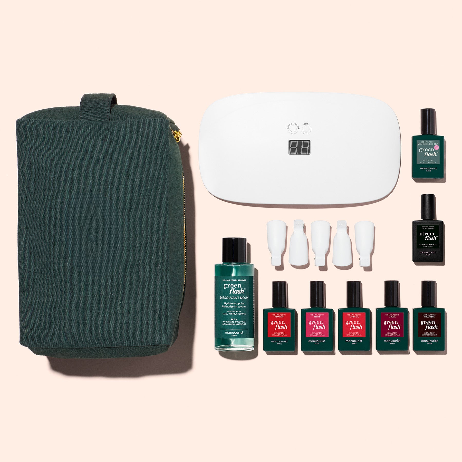 A flat lay of Manucurist’s Super Starter Kit—featuring a green zippered pouch, white LED lamp, nail polish bottles, nail tools, and solution—arranged on a beige background for an ultra-glossy manicure or DIY gel kit.