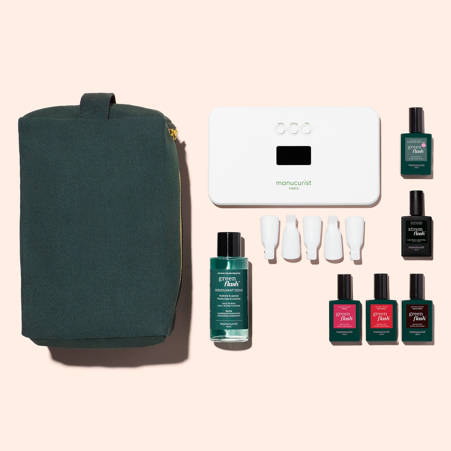The Manucurist Starter Kit includes a dark green zip pouch, white LED nail lamp, Vitaminized Base Coat, four white nail caps, and six bottles for a glossy manicure—all displayed on a beige background.