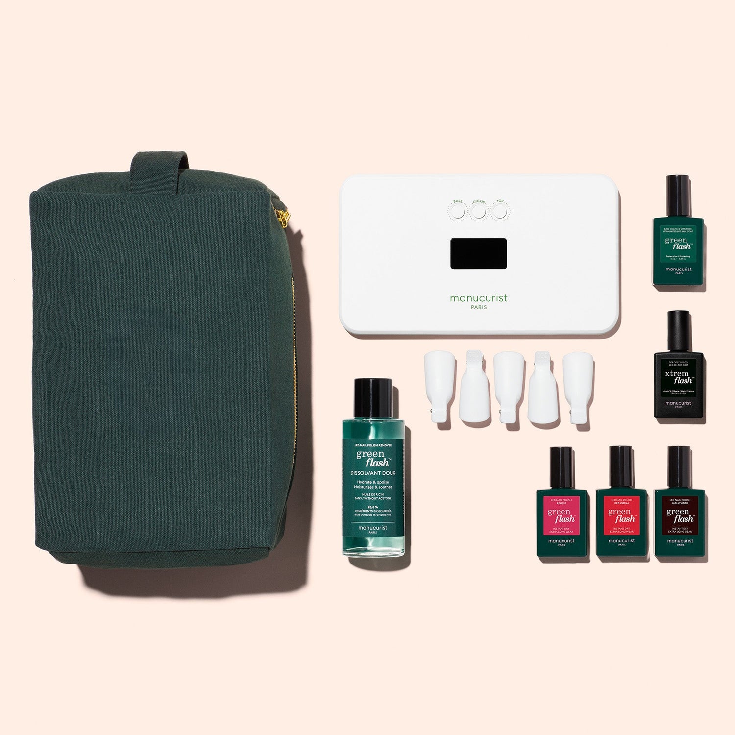 The Manucurist Starter Kit includes a dark green zippered pouch, white manicure lamp, remover, four white nail caps, and six bottles—one is a vitaminized base coat—for an ultra-glossy manicure on a pale pink background.