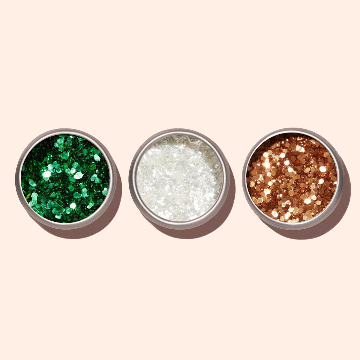 Three round Manucurist containers filled with chunky glitter for nail art are arranged side by side on a beige background. The left holds green, the center copper biodegradable glitter, and the right gold.