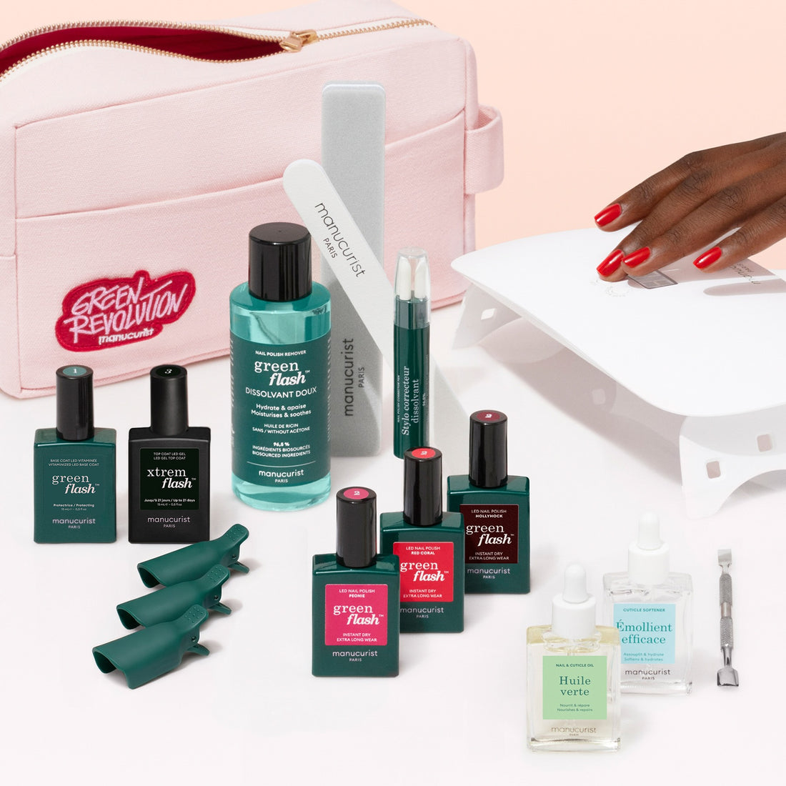 Presenting the Addict Kit by Manucurist—a comprehensive set featuring nail polishes, a Vitaminized Base Coat, nail files, cuticle oils, remover, gel polish, a mini LED lamp, and a stylish pink case. The kit is showcased with a hand displaying ultra-glossy polished red nails.