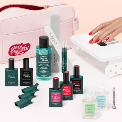 A flat lay of the Manucurist Addict Kit, featuring gel polish, a Vitaminized Base Coat, remover, nail files and tools, green finger clips, a small pink bag, and a UV lamp, with a hand receiving an ultra-glossy red gel manicure.