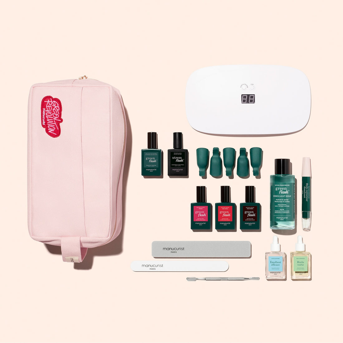 The Manucurist Addict Kit is arranged neatly on a beige background, featuring a pink pouch, an LED nail lamp, six bottles of ultra-glossy gel polish, a nail serum pen, two nail files, a cuticle pusher, and three small bottles—including the Vitaminized Base Coat.