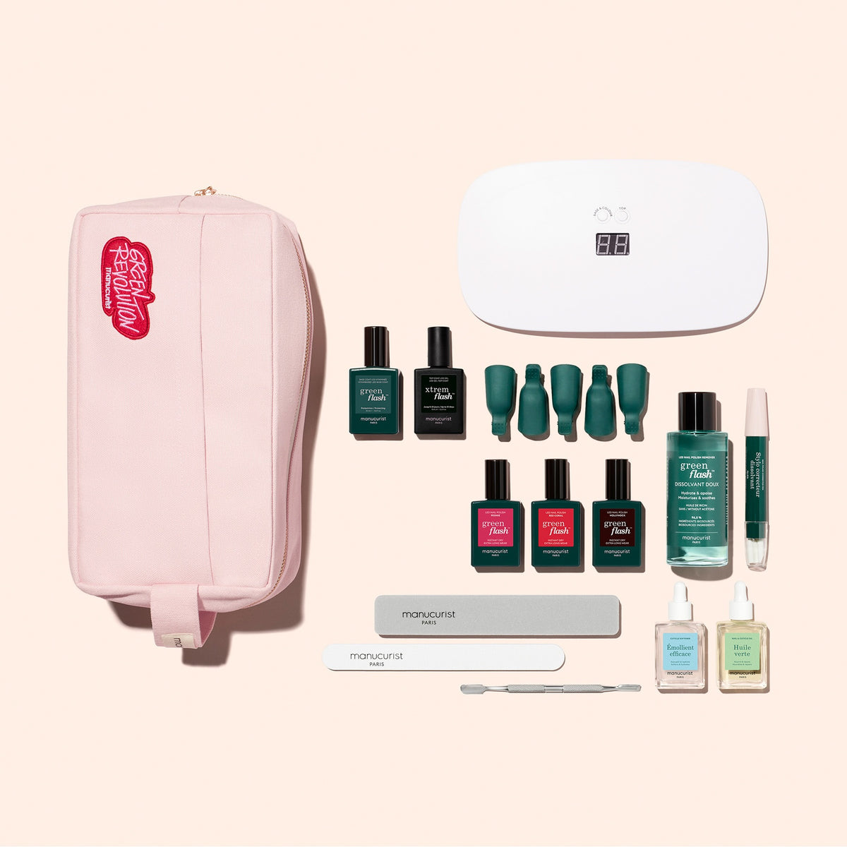 The Manucurist Addict Kit is arranged neatly on a beige background, featuring a pink pouch, an LED nail lamp, six bottles of ultra-glossy gel polish, a nail serum pen, two nail files, a cuticle pusher, and three small bottles—including the Vitaminized Base Coat.