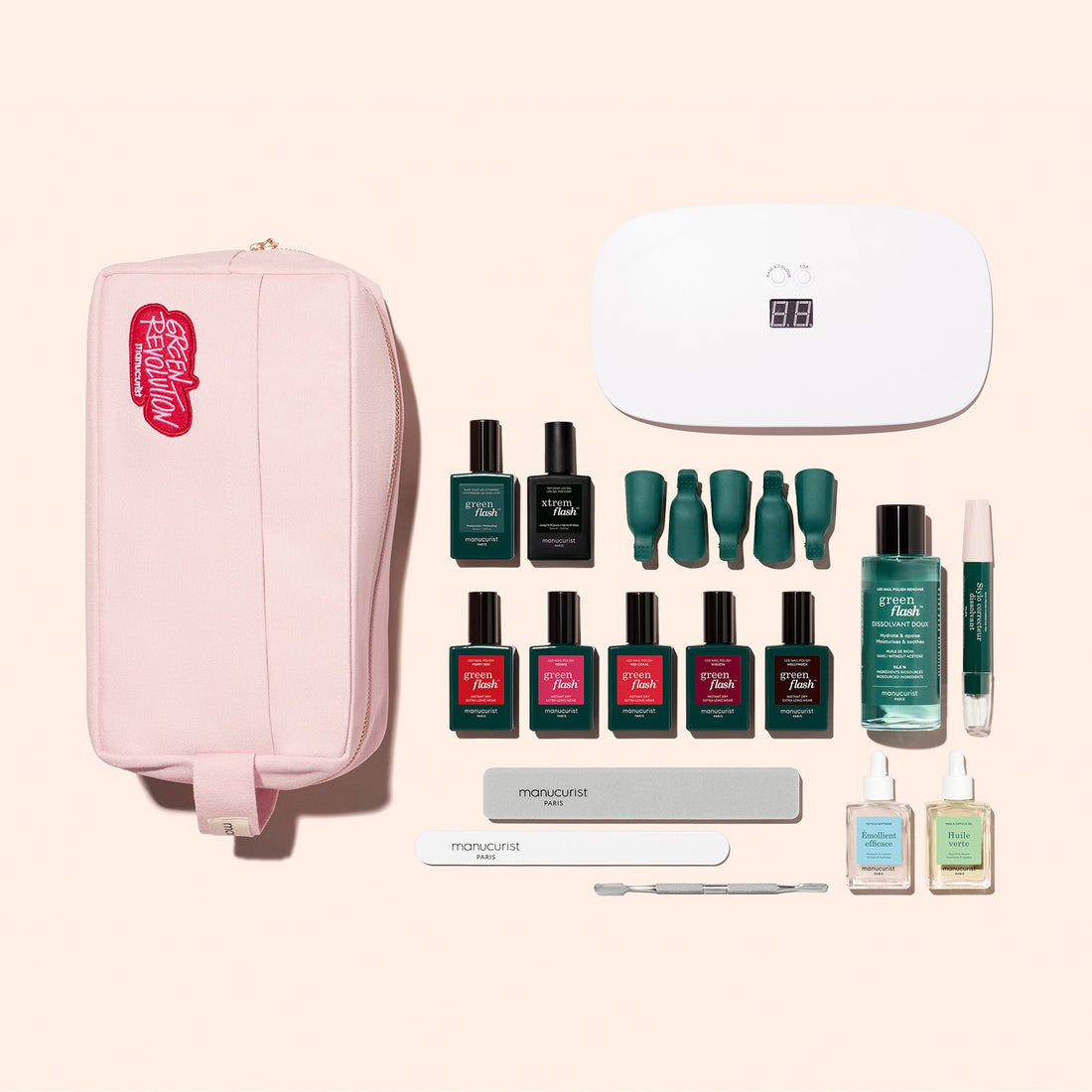 The Manucurist Super Addict Kit—including a pink pouch, Green Flash gel polish, nail tools, files, remover bottles, and a white LED nail lamp—is neatly arranged on a light beige background, making it perfect for achieving an ultra-glossy manicure at home.