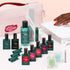 A hand with red nails is near a UV lamp. The Manucurist Super Addict Kit, featuring various green and pink manicure bottles—including Green Flash gel polish and Vitaminized Base Coat—along with nail tools and a pink bag labeled “Green Revolution,” is arranged on a white surface for an ultra-glossy manicure.