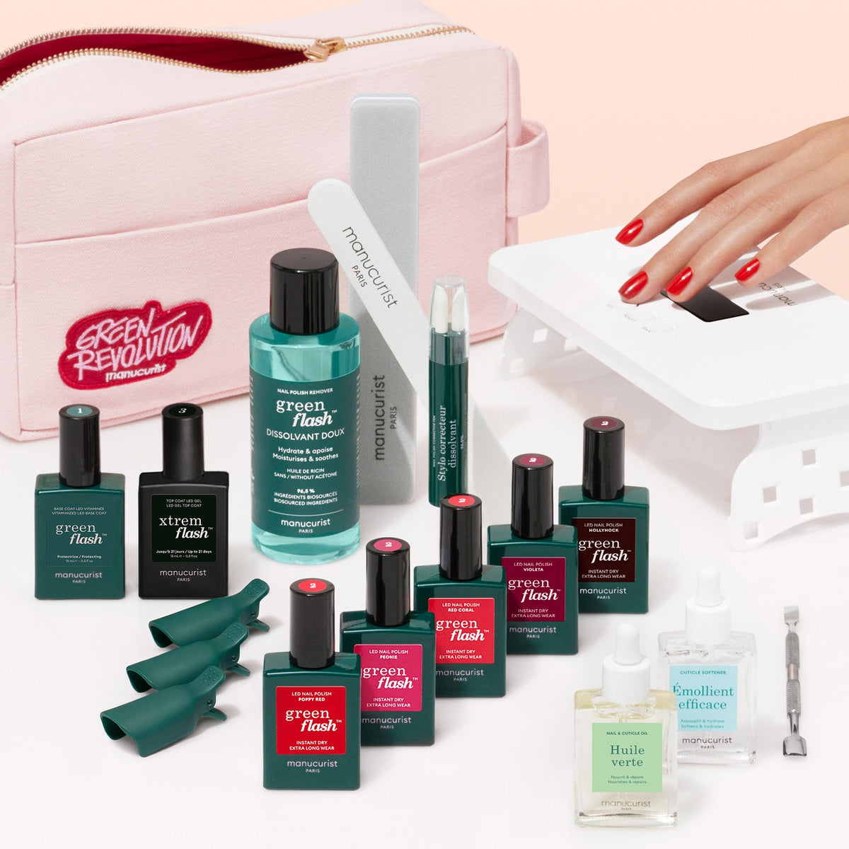 Introducing the Manucurist Super Addict Kit: a pink manicure kit bag filled with green and red Green Flash gel polish bottles, must-have nail care tools, remover, nourishing oils, a LED lamp, plus a hand shown using the lamp with glossy red nails. This complete set provides everything you need for an ultra-glossy, salon-quality manicure at home—including essentials like Vitaminized Base Coat and long-lasting Green Flash gel polish.