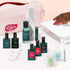 A hand with red polished nails, prepped with Manucurist Addict Kit, reaches under a white lamp. Around it are gel polish bottles, manicure tools, nail care items, and a pink bag featuring the Green Revolution slogan.