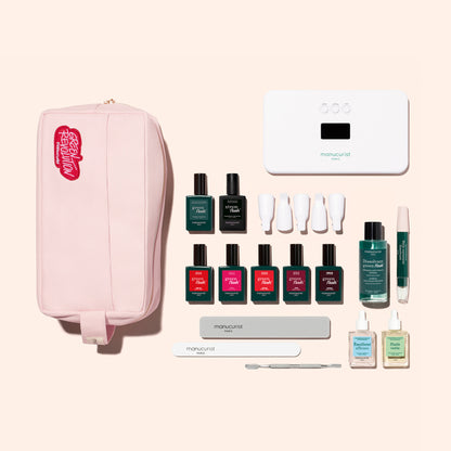 The Manucurist Super Addict Kit, featuring an LED nail lamp, polishes, tools, and accessories, is arranged on a beige background.