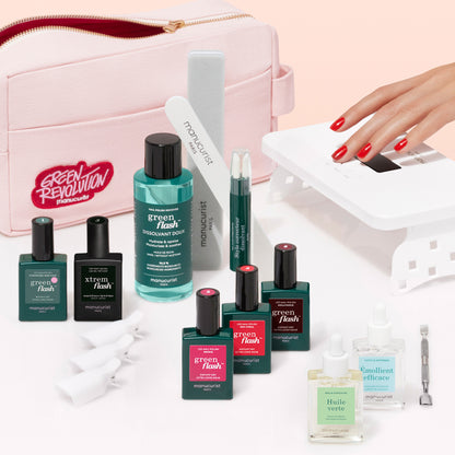 The Manucurist Addict Kit features Green Flash gel polish, vitaminized base coat, remover, oils, files, a cuticle tool, and a UV lamp beside a pink pouch. A hand with red nails is under the lamp for a glossy manicure on a white surface.