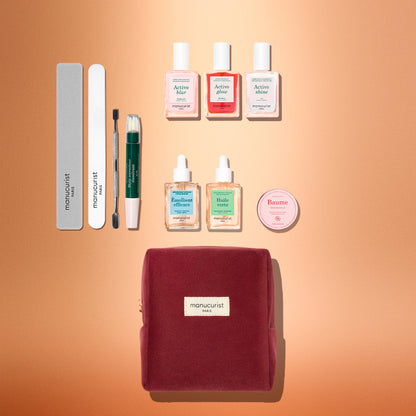 The Manucurist Active™ Ultimate Kit Gift Set features three nail polishes, two dropper bottles, a round balm tin, two nail files, a cuticle pusher, and a correction pen arranged above a velvet cosmetic bag.
