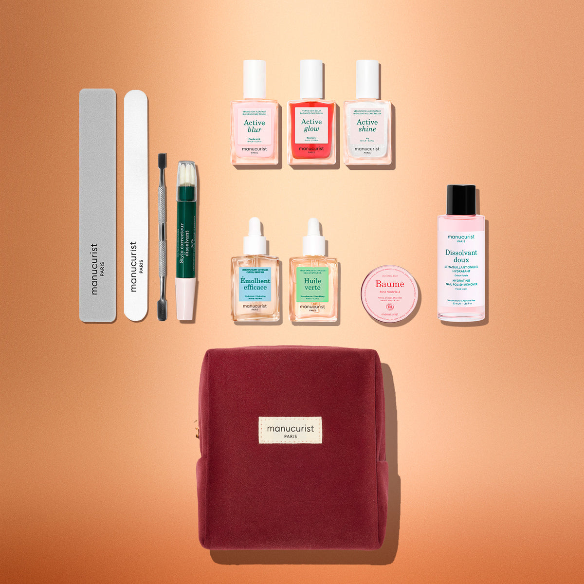 The Manucurist Active™ Ultimate Kit Gift Set featuring three polish bottles, two droppers, balm, remover, two files, a cuticle pusher, and a correction pen arranged above a maroon pouch for a complete manicure routine.