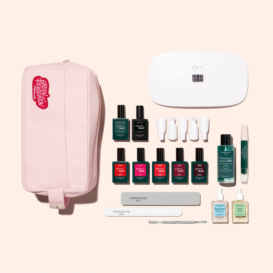 The Manucurist Super Addict Kit includes a pink zippered pouch, Green Flash gel polishes in assorted colors, a white LED lamp, remover bottles, nail files, manicure tools, and four white polish caps on a light background.