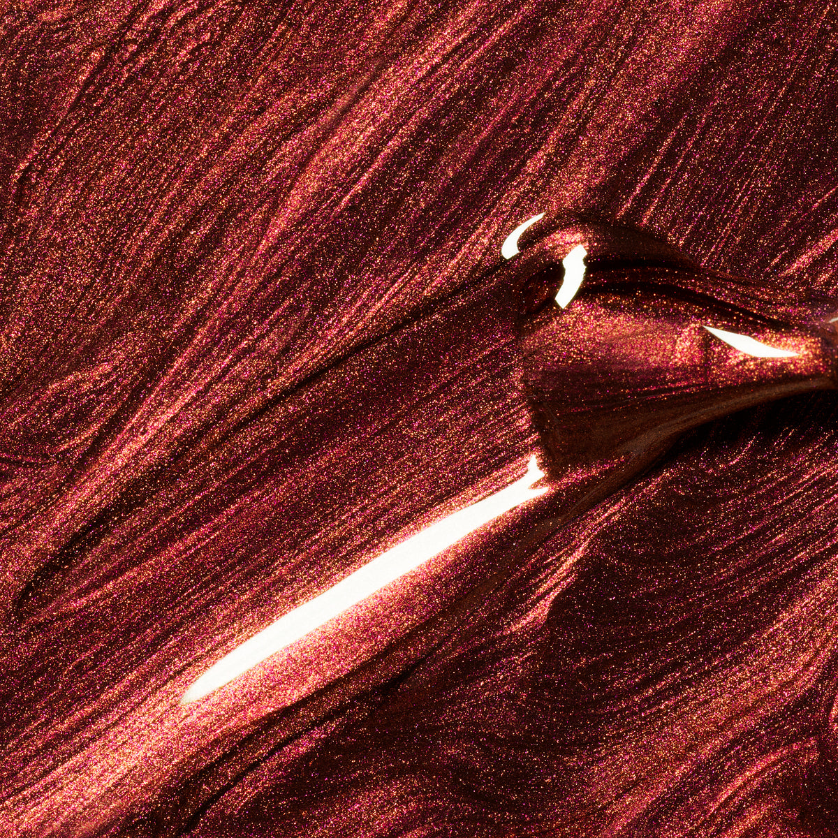A close-up of Manucurist Utopia gel polish, a shimmering metallic crimson shade, being spread with a brush to reveal textured, glistening streaks and glossy highlights.