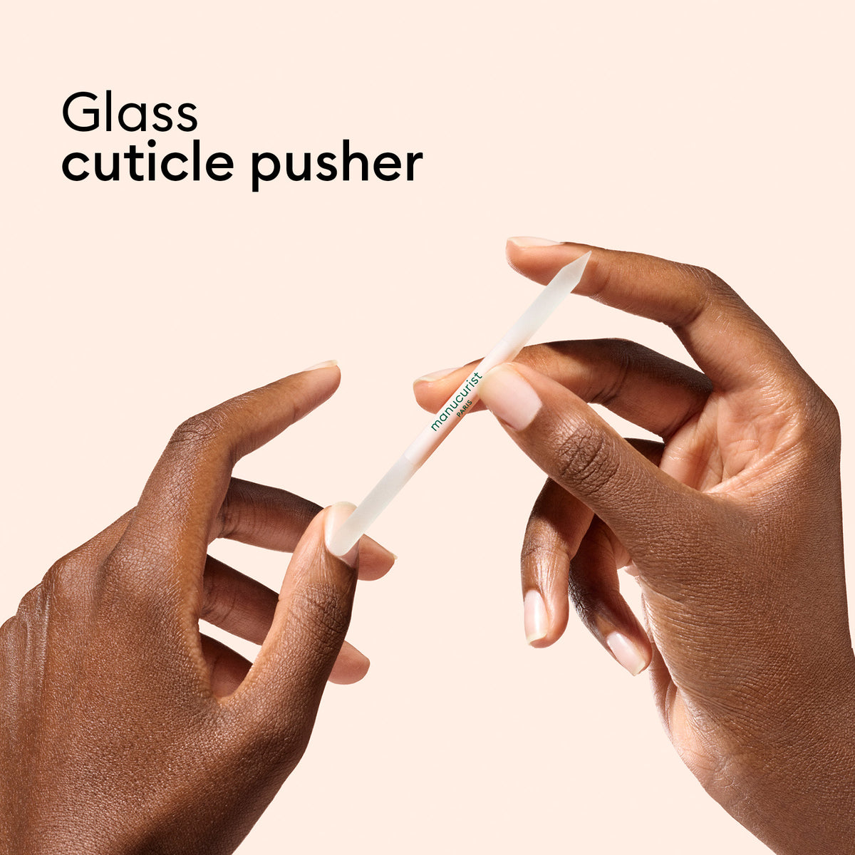 Two hands hold a tool from the Manucurist Glass Nail Accessory Trio against a light beige background, with “Glass Nail Accessory Trio” in the upper left corner. Pair these for flawless nail care.