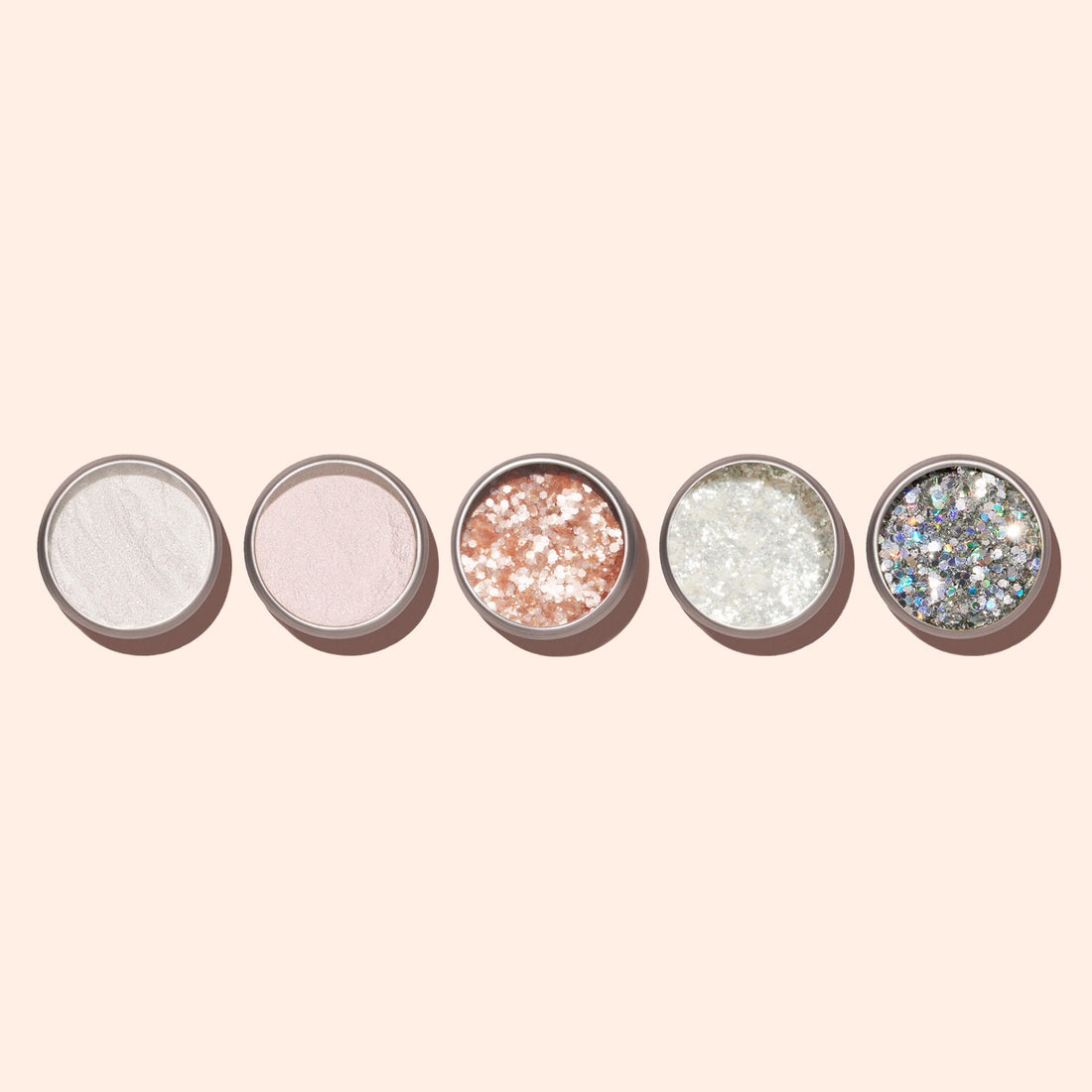 Five round Manucurist Blush biodegradable glitter containers, ideal for nail art, are lined up on a beige background. Their textures and colors range from white and pale pink sparkle to gold and silver glitter.