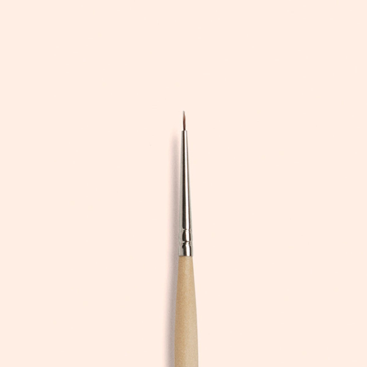 The Manucurist Fine Tip Brush, made with vegan synthetic bristles and a wooden handle, stands vertically against a light beige background—ideal for precision nail art.